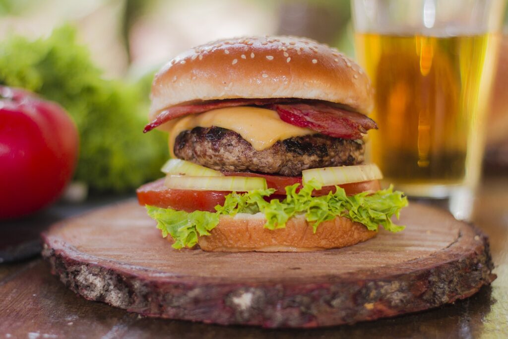 A hamburger with bacon, lettuce and tomato on top of a wooden board.