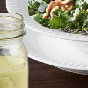 A jar of juice next to a bowl of salad.