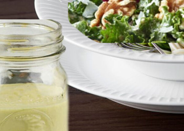 A jar of juice next to a bowl of salad.